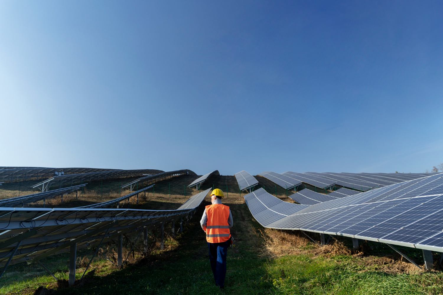 Field engineer in a hard hat and safety vest walking between rows of solar panels